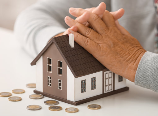 Elderly woman with figure of house and coins at table, closeup. Concept of payment for utility services